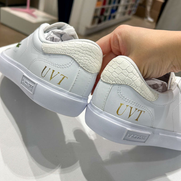 Gold foil initials applied by hand on white Lacoste sneakers during a live heat foiling personalization event in Toronto.