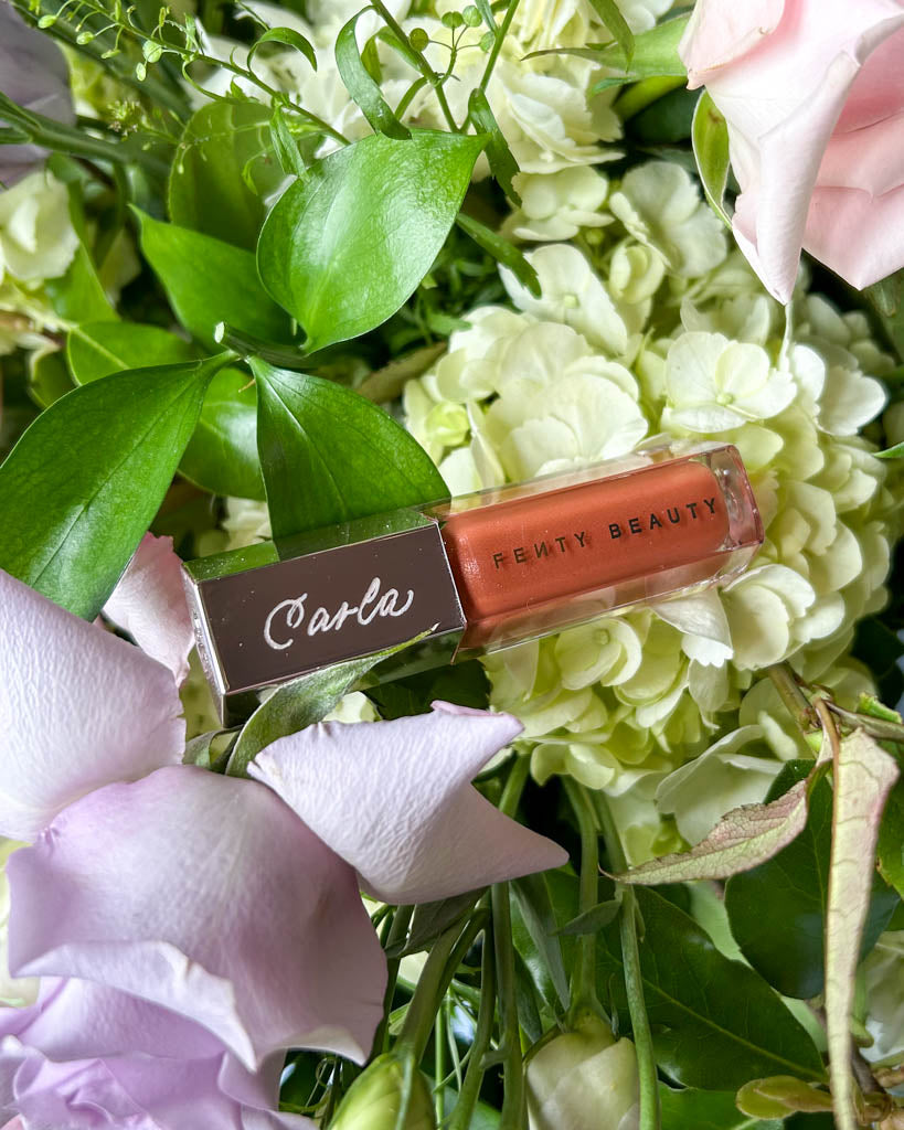 Personalized Fenty Beauty lip gloss engraved with the name “Carla,” styled among pastel florals for a Toronto bridal event by JW Lettering.