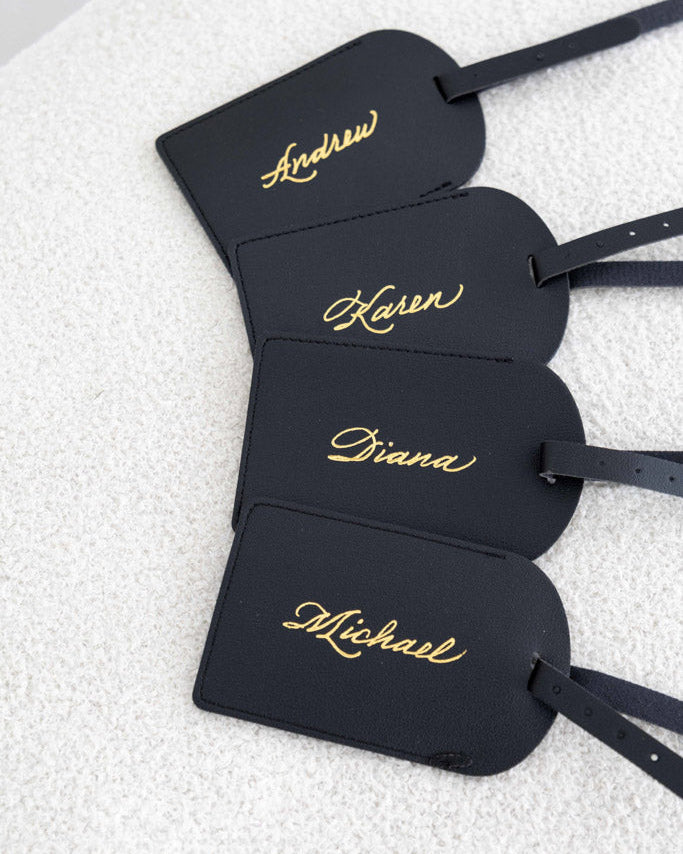 Black leather luggage tags personalized with gold foil names in script calligraphy using JW Lettering’s in-studio heat foiling technique in Toronto.