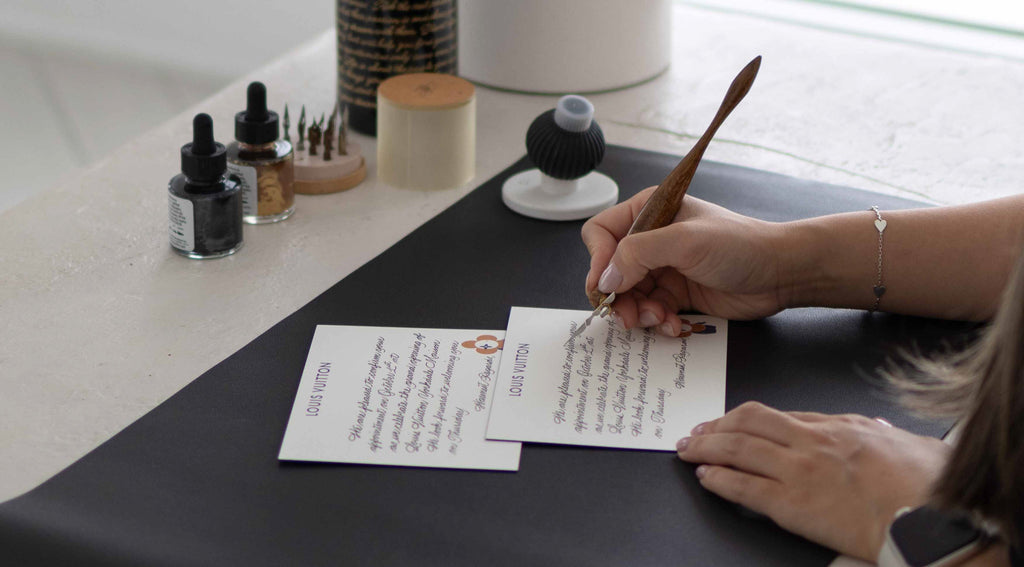 Toronto calligrapher Jessie Wang of JW Lettering handwrites personalized Louis Vuitton cards using a dip pen and black ink during a luxury brand event, showcasing her elegant live calligraphy technique.