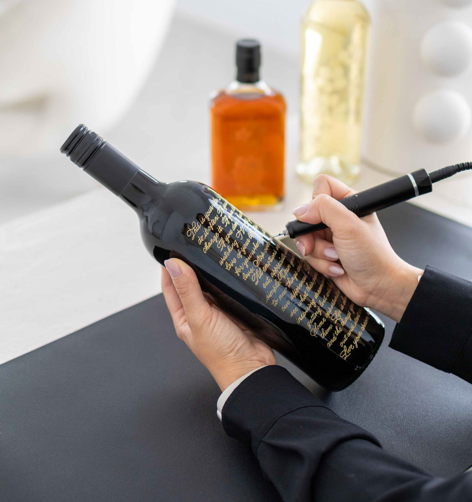 Gold calligraphy engraving process on a black wine bottle in Toronto studio.