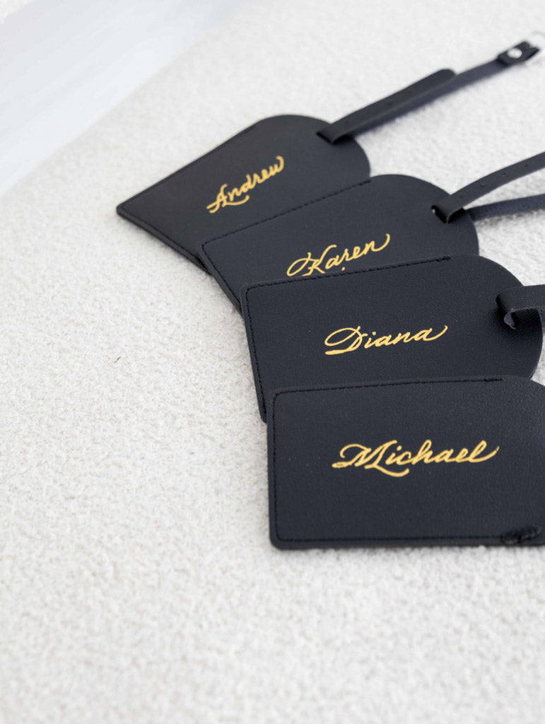 Black leather luggage tags personalized with gold foil calligraphy.