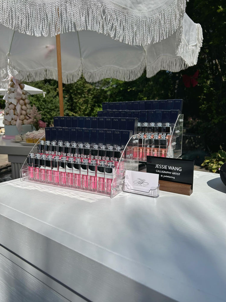 Toronto wedding live calligraphy and engraving setup with Dior lip gloss baby shower guest gifts under white parasol.